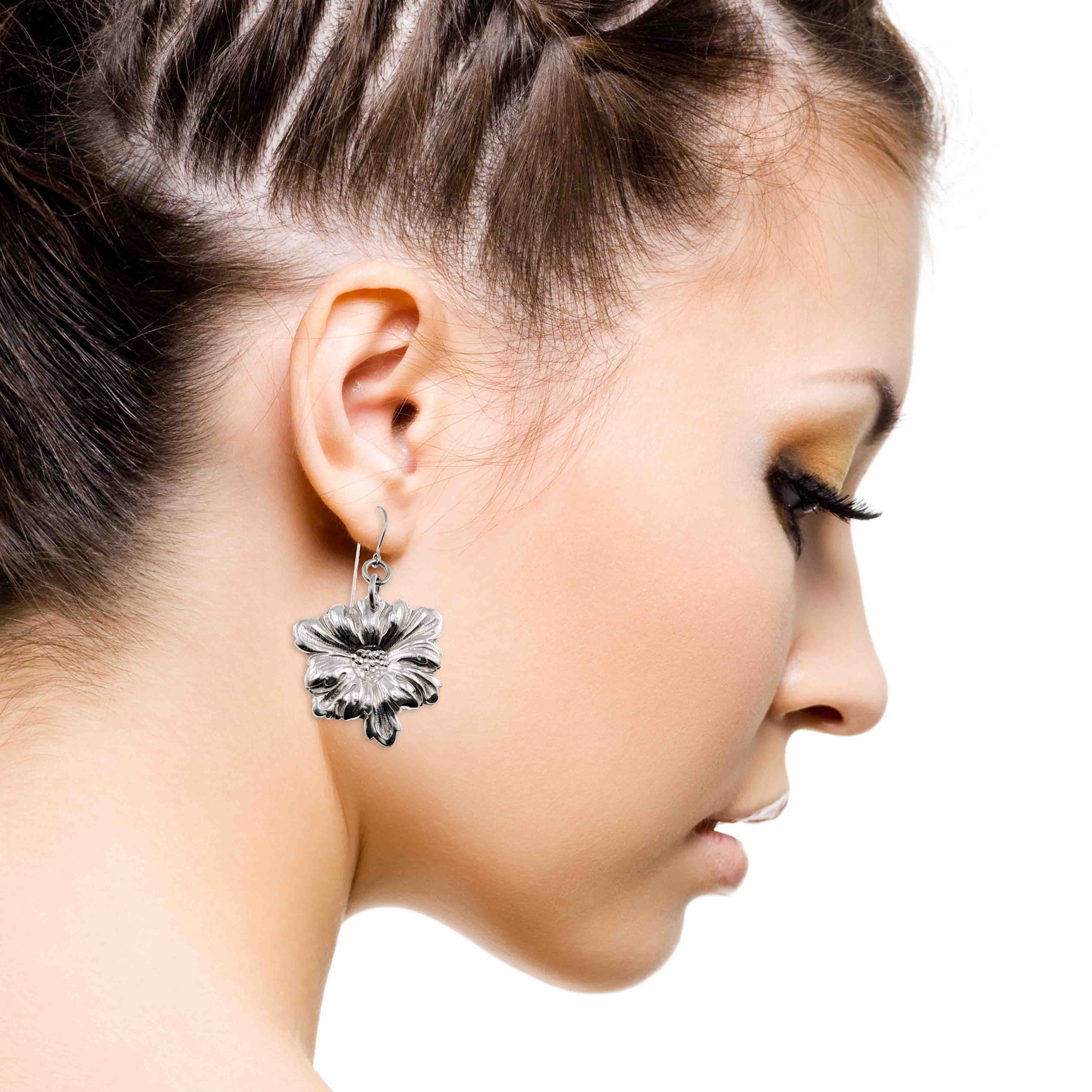 6 of 7: Close-up of a woman wearing a silver floral earring on a white background