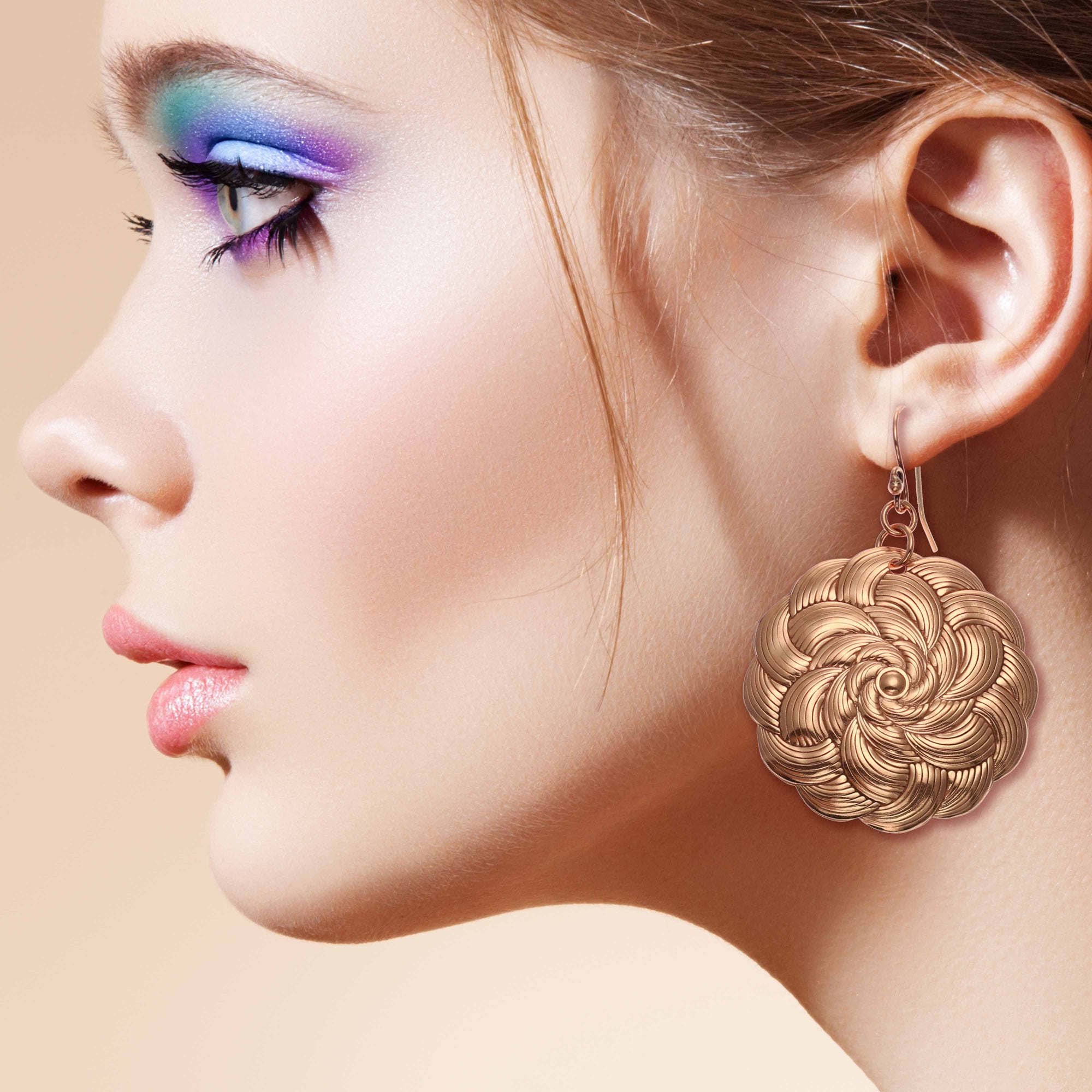 A woman with vibrant makeup and stylish Copper Mandala Disc Earrings, showcasing her unique and colorful style.