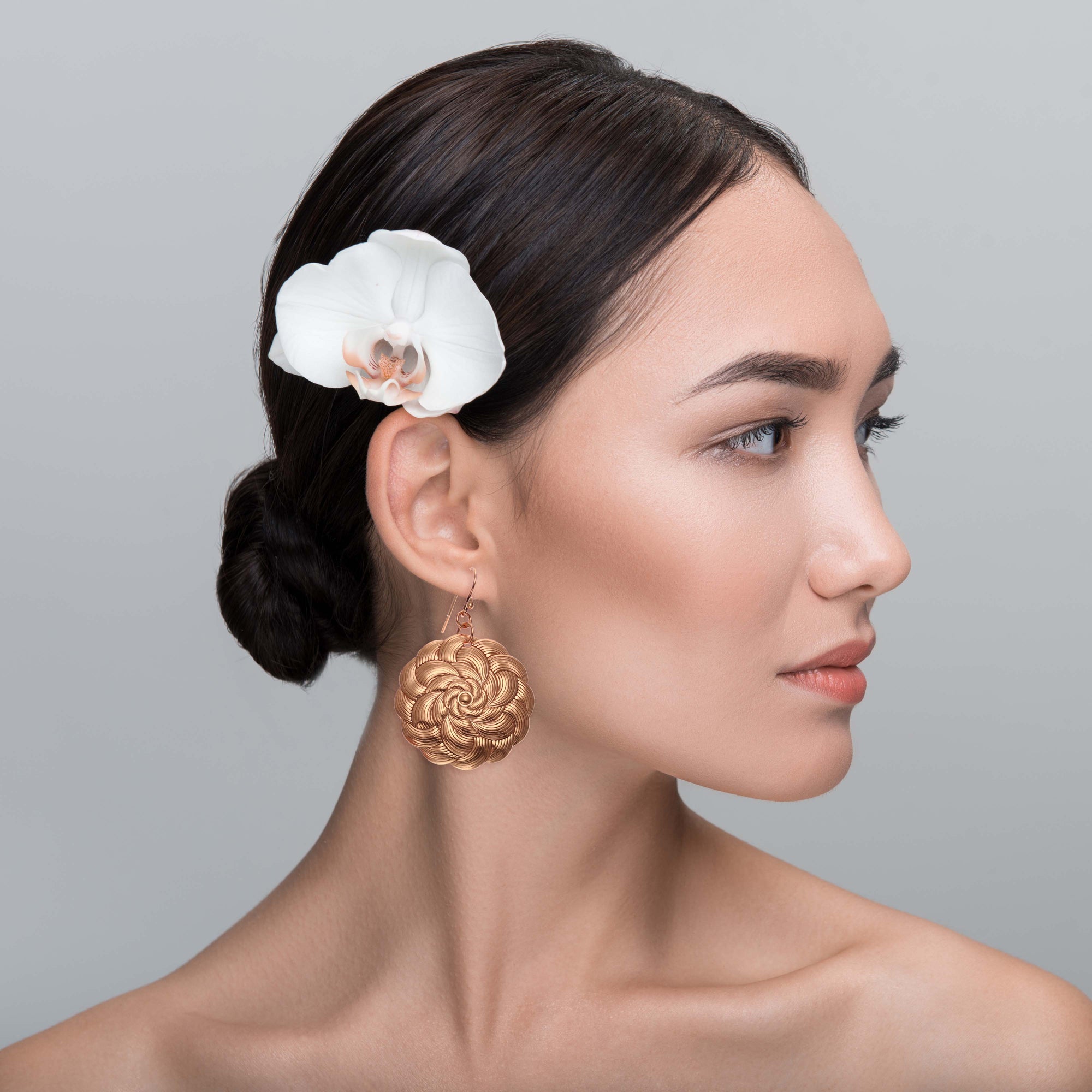 A woman with a flower in her hair wearing Copper Mandala Disc Drop Earrings, radiating elegance and grace.