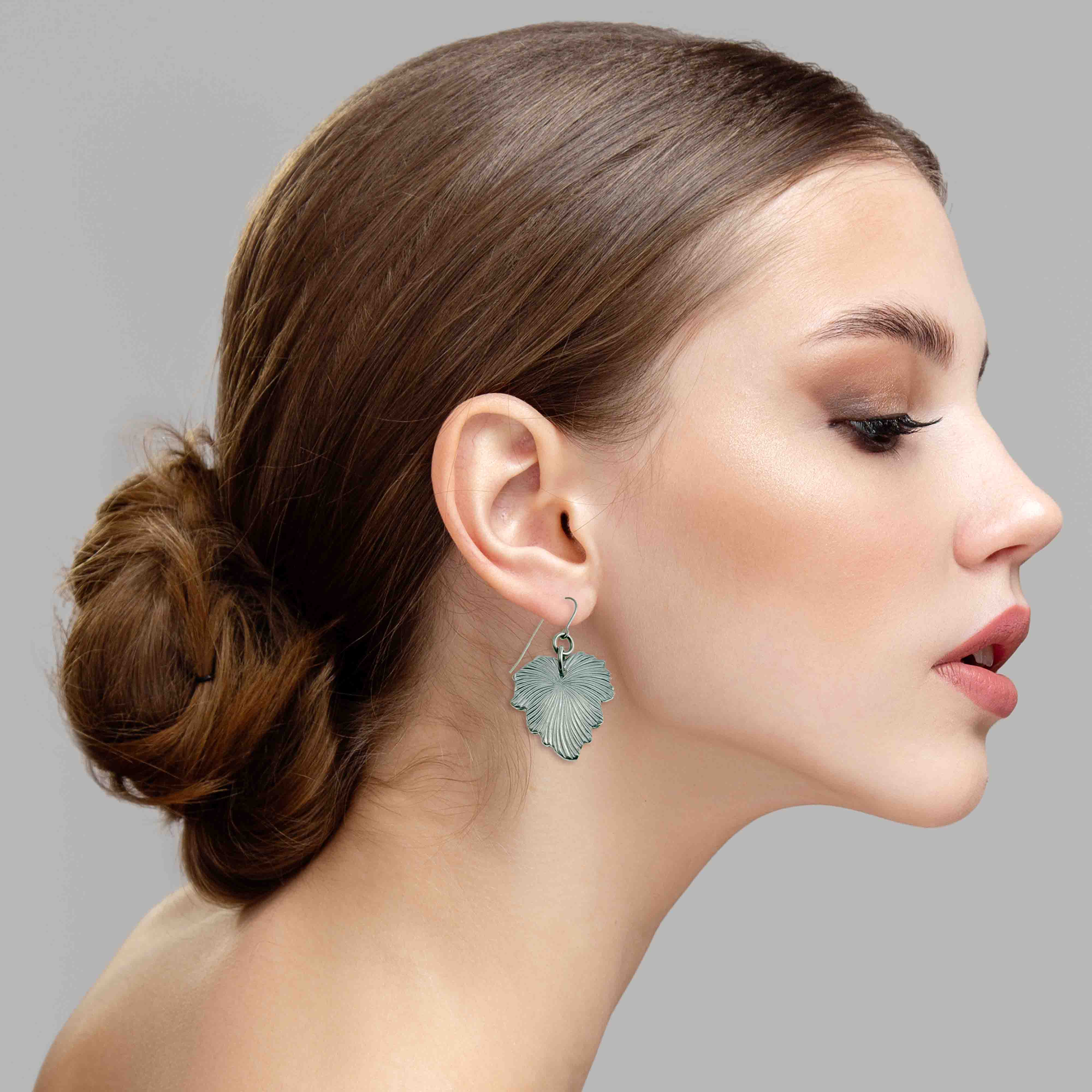 6 of 7: Woman wearing a silver Grape Leaf Aluminum Dangle Earrings against a gray background