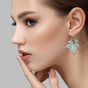 2 of 7: Close-up of a woman wearing a Medium Maple Leaf Aluminum Dangle Earring against a gray background