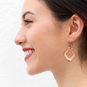 6 of 8: A Smiling Woman Wearing Medium Pierced Copper Clover Drop Earrings