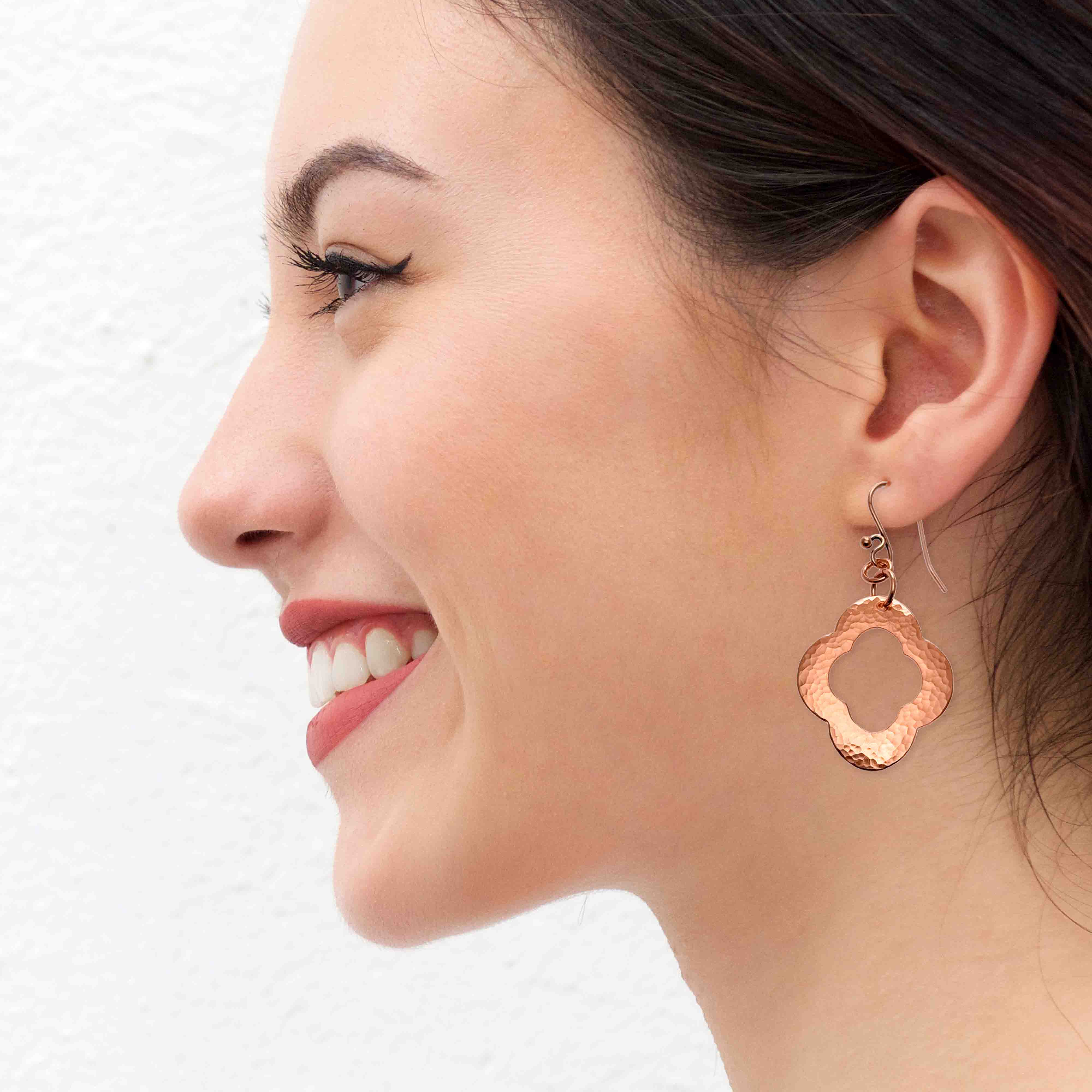 6 of 8: A Smiling Woman Wearing Medium Pierced Copper Clover Drop Earrings