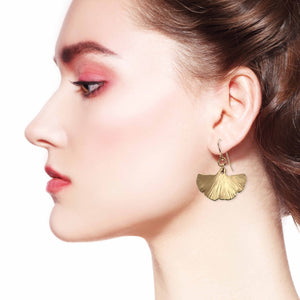 6 of 7: Side view of woman wearing bronze ginkgo leaf drop earrings.