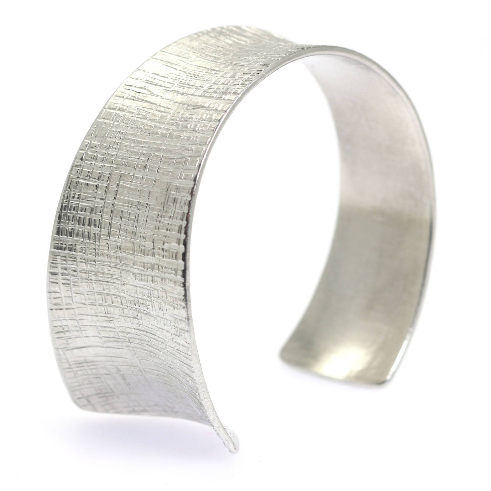 An Anticlastic Tapered Linen Aluminum Bangle Bracelet on a White Background