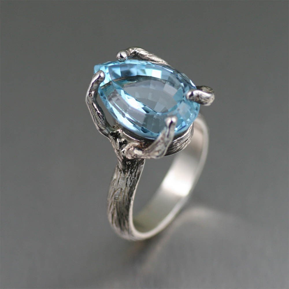 Sterling silver ring with an organic tree branch band, holding a pear-cut Swiss blue topaz gemstone in an airy, twig-style prong setting.