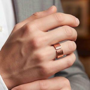 8 of 9: Hand wearing a polished copper bark texture open cuff ring with squared ends, styled with a light gray jacket and white shirt for a refined everyday menswear look.