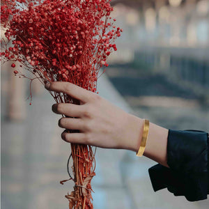 4 of 9: Hand holding a bouquet of red dried flowers wearing 10mm Wide Bark Nu Gold Tone Brass Cuff Bracelet with a blurred background