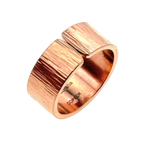 3 of 8: Angled product image of a handmade solid copper cuff ring on a white background. The ring features a wide open band with rounded edges, a hand chased exterior with fine linear texture, and a polished inner surface stamped “JSBrana” and “COPPER.” Its warm rose copper color and bold 10mm width give it a clean, modern artisan look.