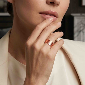 4 of 8: Close up lifestyle image of a woman wearing a wide copper cuff ring on her finger while lightly touching her lips. The handmade ring has an open back, a polished shine, and a hand chased texture with fine linear markings. She wears a soft ivory blazer, and the blurred indoor background gives the warm copper ring a clean, modern, elegant look.