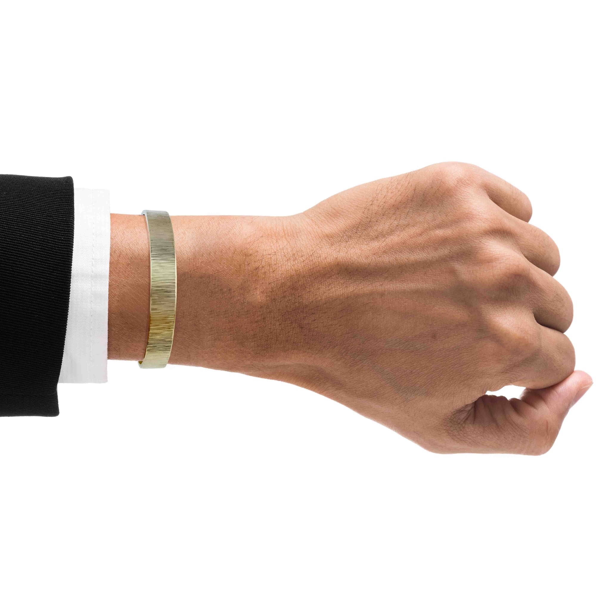 A Man's wrist wearing a 10mm Wide Chased Nu Gold Tone Brass Cuff Bracelet on a white background