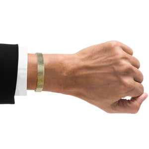 2 of 9: A Man's wrist wearing a 10mm Wide Chased Nu Gold Tone Brass Cuff Bracelet on a white background