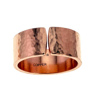 7 of 9: Front view of a wide hammered copper cuff ring with an open center gap, showing a polished finish and textured surface that reflects light. The interior of the ring is smooth and stamped with “COPPER,” with warm reddish tones visible along the inner band.