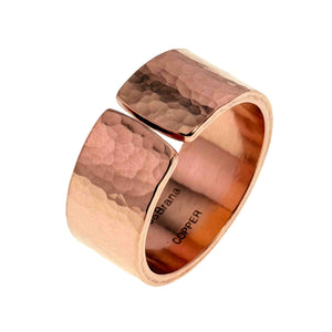 5 of 9: Angled view of a wide hammered copper cuff ring with an open front design, featuring a polished finish that reflects light across its textured surface. The warm copper tone shows subtle variations, and the smooth interior is stamped with “JSBrana COPPER,” highlighting its handcrafted look.