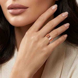 8 of 9: Close up of a woman wearing a wide hammered copper cuff ring on her finger, featuring a polished finish and open front design. Her hand is gently raised near her face, showing soft neutral makeup and a beige outfit, while the ring’s warm copper tone and textured surface catch the light for a refined, modern look.
