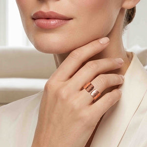 6 of 9: Close up of a woman wearing a wide hammered copper cuff ring on her finger, featuring a polished finish and open design. Her hand rests gently against her chin, highlighting the ring’s warm tone and textured surface, paired with soft neutral clothing for an elegant, modern look.