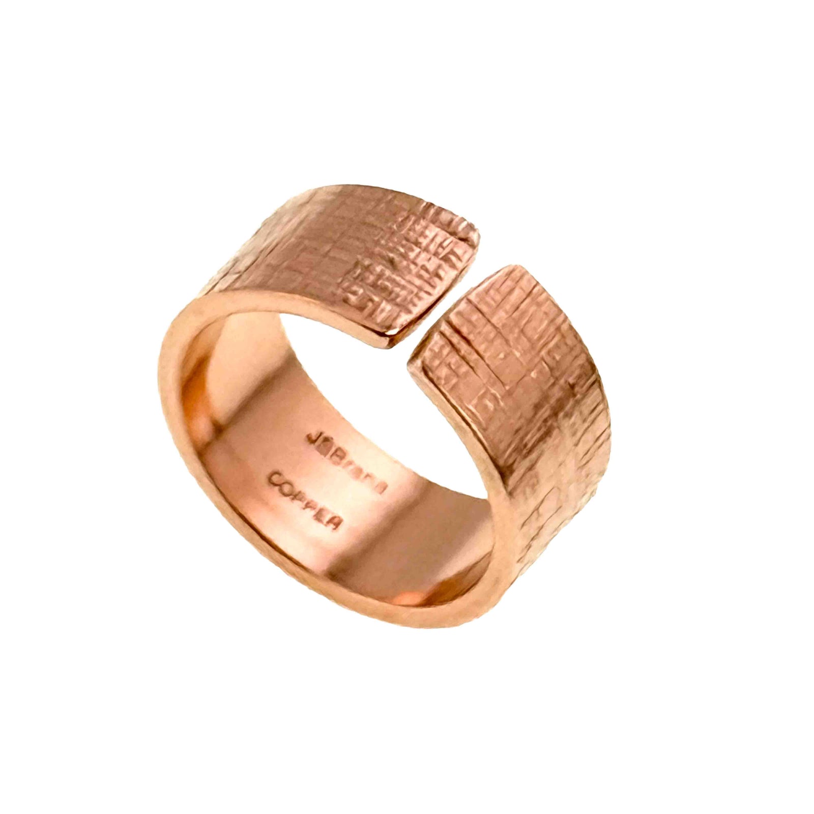 Wide 10mm open copper cuff ring with a subtle linen-like textured surface and polished interior engraved with the designer’s hallmark, shown against a plain white background.