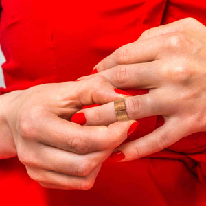 4 of 8: A close-up of a woman wearing a bold red dress and matching red nail polish, slipping on a wide copper cuff ring with a linen-textured finish. The ring features an open-front design and a warm, aged copper tone, standing out against her vibrant outfit.