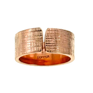 6 of 8: A close-up image of a handcrafted copper cuff ring featuring a wide 10mm band with a linen-textured finish and an open-front design. The warm reddish hue of the raw copper contrasts with the engraved "COPPER" stamp on the inner band.