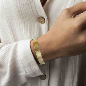 4 of 9: 10mm Wide Linen Nu Gold Tone Brass Cuff Bracelet on a Woman's wrist with a white shirt background