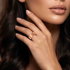 4 of 9: Close-up of a woman’s hand wearing a matte copper cuff ring with a wide open band and smooth brushed finish, styled on the finger near her face, with soft makeup, glossy lips, and dark wavy hair in the background.