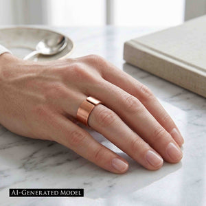8 of 9: Close-up of a hand resting on a light marble surface wearing a matte copper cuff ring with a wide open band and smooth brushed finish, styled in a calm indoor setting with a book and soft neutral tones in the background.  AI Generated Model.