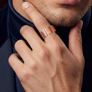 8 of 9: Close-up of a hand wearing a matte copper cuff ring with a wide open band and brushed finish, styled on the finger near a man’s face with light stubble, creating a modern, minimal look against a dark background.