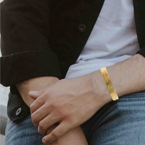 2 of 9: Model wearing a wide textured Nu Gold brass cuff bracelet on the wrist, shown in a casual outfit to demonstrate scale, fit, and warm golden finish.