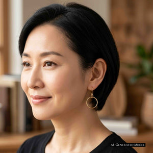 4 of 8: AI generated model with short black hair wearing a 1 inch chased bronze hoop earring indoors. The polished bronze hoop hangs from a French ear wire beside her jaw and is paired with a simple black top. A softly blurred warm interior appears in the background.