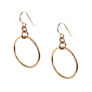7 of 8: Angled view of a pair of handmade 1 inch chased bronze hoop earrings on a white background. Each polished bronze hoop shows the hand chased edge texture, connecting rings, and curved bronze French ear wire, giving a clear view of the earrings from a three quarter angle.