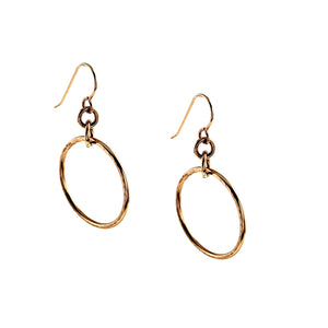 7 of 8: Pair of 1 inch hammered bronze hoop earrings shown at an angled side view on a white background. Each earring features a warm polished bronze hoop suspended from small connecting rings and a bronze French ear wire, highlighting the handmade texture and open circular shape.
