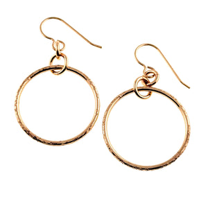 1 of 8: Pair of polished bronze hoop earrings shown from the front and back against a white background. Each one inch round hoop has a hand textured rim, small connecting rings, and a bronze French ear wire. Gold text identifies the front and back views.