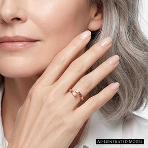 2 of 9: Close up of a woman with gray hair wearing a narrow copper bypass ring with a bark texture. The ring sits on her finger as she raises her hand near her cheek. A pale manicure and light clothing give the image a clean, polished look.  AI Generated Model.