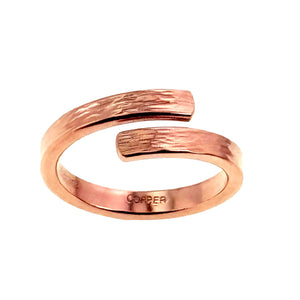 3 of 9: Front view of a slim solid copper bypass ring on a white background. The open wrap design curves around the band and ends in two flat bark textured tips. The inside of the ring is stamped with the word copper.