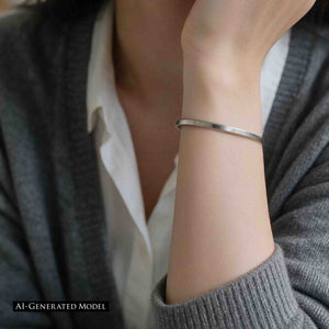 8 of 10: AI generated female model wearing a slim brushed stainless steel cuff bracelet with a gray knit cardigan and white top. The close view focuses on her raised wrist, showing the narrow matte silver tone bracelet against a soft neutral outfit.