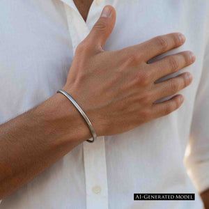 2 of 10: AI generated male model wearing a slim brushed stainless steel cuff bracelet with a white button front shirt. The close view of his hand and wrist shows the narrow silver tone bracelet paired with a simple warm weather outfit.