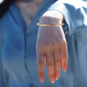 4 of 9: A Woman's wrist wearing a 3.5mm Chased Bronze Cuff Bracelet  with a blurred blue background
