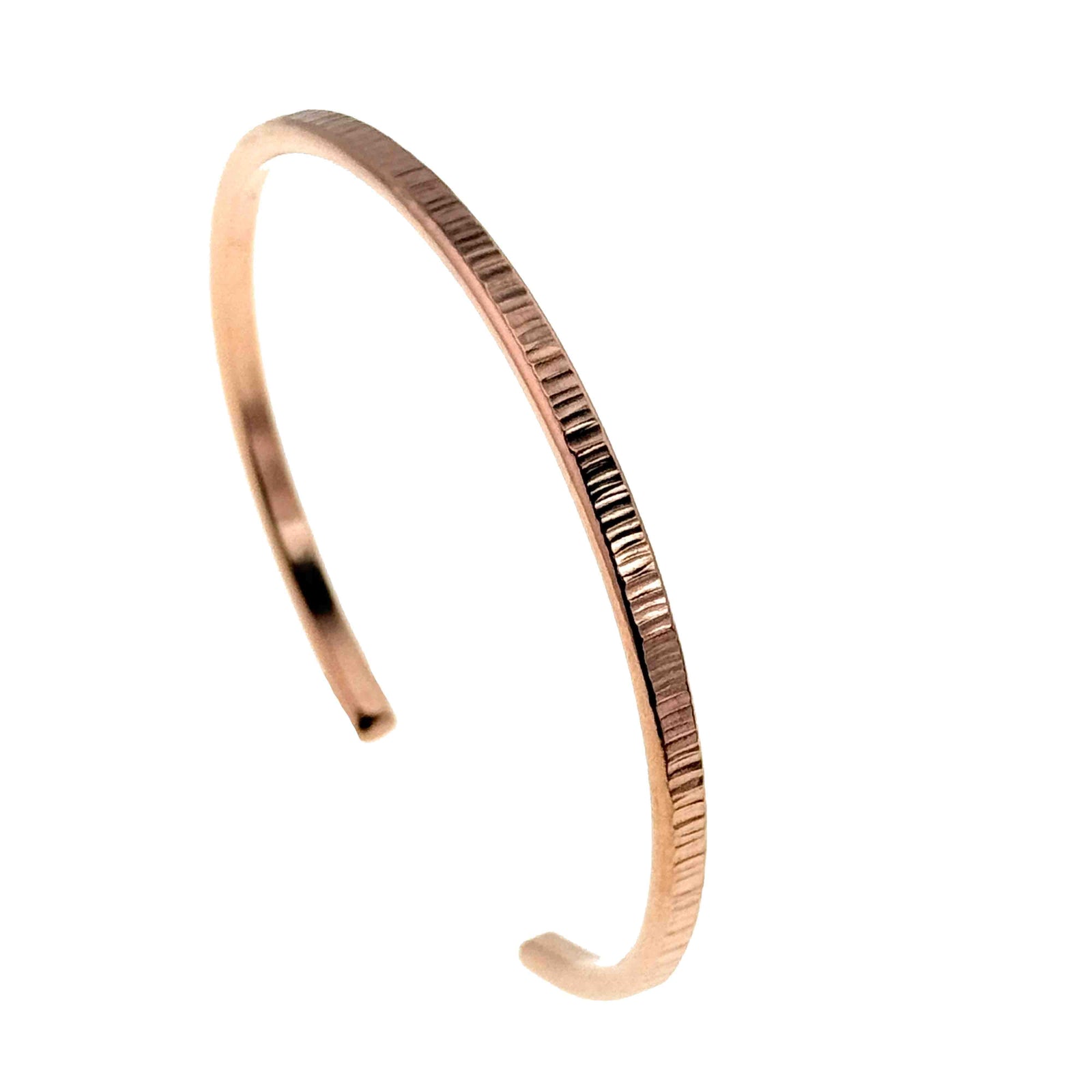 Slim 3.5mm chased copper cuff bracelet shown on a white background, photographed at an angle to highlight its softly curved open design and narrow profile. The bracelet has a warm rose copper tone with fine vertical chisel marks along the outer edge, giving it a subtle textured sparkle and minimalist, stackable look for a small to medium wrist.