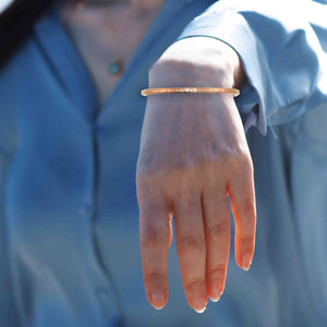 4 of 11: A woman wearing a slim, hand-textured copper cuff bracelet on their wrist, styled with a light blue blouse, with the bracelet resting just above the wrist bone and catching natural sunlight.