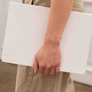 6 of 11: A person wearing a slim, hand-textured copper cuff bracelet while holding a white laptop, dressed in neutral-toned pants, showcasing a minimalist and professional style.