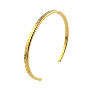 3 of 9: Close-up image of a handcrafted 3.5mm wide Nu Gold brass cuff bracelet with a chased texture. The bracelet features a slim, open-ended design and a warm golden hue. Its lightly ridged surface reflects light, adding a subtle shimmer. Displayed against a clean white background, highlighting the bracelet’s elegant simplicity and artisan finish.