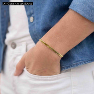 6 of 9: Close-up of a woman's wrist wearing a 3.5mm chased Nu Gold brass cuff bracelet with a subtle ridged texture and warm golden tone. The hand is casually placed in the pocket of white pants, paired with a light denim jacket, creating a relaxed, stylish look. The bracelet’s minimal design adds a touch of shine, making it an easy everyday accessory.  AI Generated Model.