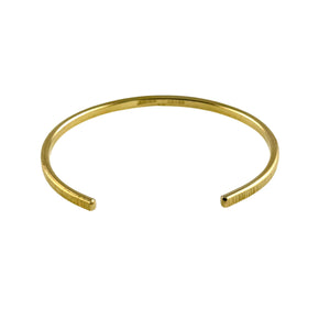 7 of 9: Angled view of a 3.5mm wide Nu Gold brass cuff bracelet with an open-ended design and lightly chased texture along the surface. The bracelet has a smooth, curved shape with a warm golden tone, highlighting its handcrafted, minimalist style. Shown against a white background, emphasizing the clean lines and subtle reflective finish.