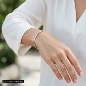 2 of 11: AI generated female model wearing the John S. Brana 3.5mm Chased Stainless Steel Cuff Bracelet with a white blouse. Close view of her extended hand and wrist shows the slim silver tone bracelet with its hand chased texture and narrow profile. The hypoallergenic 316L surgical stainless steel cuff adds a refined accent to her casual outfit against a softly blurred green outdoor background.