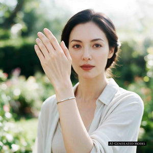 7 of 11: AI generated female model with dark hair wearing a white collared blouse and the John S. Brana 3.5mm Chased Stainless Steel Cuff Bracelet. She raises her hand beside her face, displaying the slim silver tone bracelet and its hand chased surface. The handcrafted 316L surgical stainless steel jewelry complements her relaxed style, with softly blurred trees and greenery in the outdoor background.