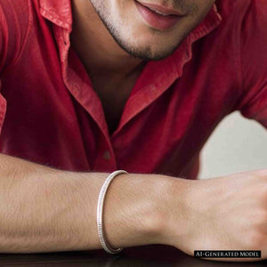 4 of 11: AI generated male model wearing the John S. Brana 3.5mm Chased Stainless Steel Cuff Bracelet with a casual red buttoned shirt. Close view of his forearm resting on a dark wooden surface highlights the narrow silver tone bracelet and hand chased texture. The slim 316L surgical stainless steel cuff provides a simple masculine jewelry accent that works with relaxed everyday clothing.
