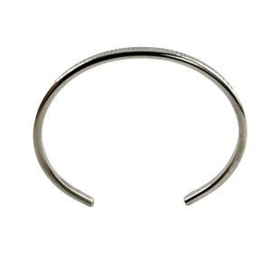 5 of 11: Overhead product photograph of the John S. Brana 3.5mm Chased Stainless Steel Cuff Bracelet showing its gently oval shape, narrow band, and open ends. The handcrafted 316L surgical stainless steel bracelet has a silver tone finish with small chased marks along the outer edge. The smooth interior and curved construction are clearly visible against a plain white background.