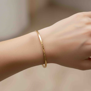 4 of 10: Close-up lifestyle image of a slim hammered bronze cuff bracelet worn on a woman’s wrist. The narrow 3.5mm solid bronze cuff features a warm golden tone with a subtle hand-hammered texture that reflects light softly. The open cuff design curves gently around the wrist for a clean, minimalist look. The background is softly blurred in neutral tones, keeping the focus on the bracelet’s simple, modern style.