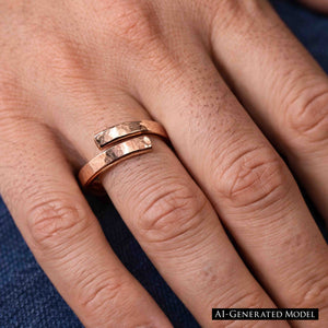 2 of 7: A close-up view of a hand wearing a 3.5mm hammered copper bypass ring on the middle finger. The ring features an open front design with two polished, textured ends that curve past each other. The warm reddish tone of the raw copper contrasts subtly against the natural skin tone. The hammered finish catches the light, giving the ring a rugged yet refined look. Blue denim fabric is partially visible in the background.  AI Generated Model.