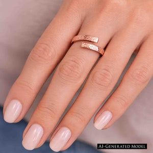 4 of 7: A close-up of a woman’s hand wearing a 3.5mm hammered copper bypass ring on the ring finger. The open-ended ring features two flat, textured copper tips that curve past each other, creating a modern wrap style. The warm rose-copper tone contrasts softly with smooth, light skin and pale pink manicured nails. The hammered finish reflects light, highlighting the handcrafted look against a neutral background.  AI Generated Model.
